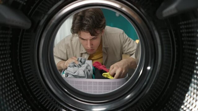 View from inside the washing machine, young man with laundry basket holds two different socks, searching for pair