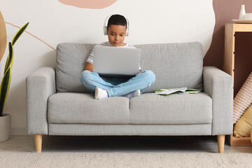 Little African-American boy with laptop studying computer sciences online at home