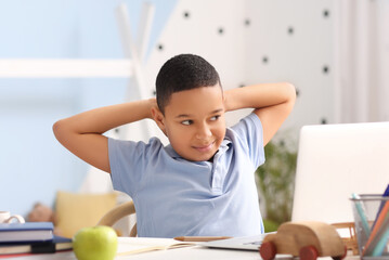 Little African-American boy studying computer sciences online in bedroom