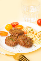 Cutlets with bulgur, boiled vegetables and tomatoes on light yellow table in kitchen