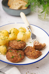 Plate with cutlets, boiled baby potatoes and dill on white grunge table in kitchen