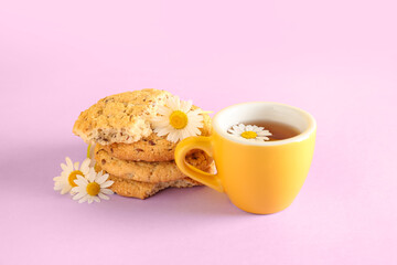 Cup of natural chamomile tea with cookies and flowers on pink table near yellow wall