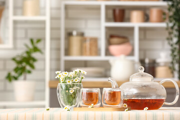 Wooden tray with teapot, cups of natural chamomile tea and flowers on table in kitchen