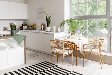 Interior of modern kitchen with white counters, island and dining table near big window