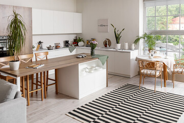 Interior of modern kitchen with white counters, island and dining table near big window
