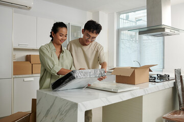 Joyful couple wrapping and packing framed photos when moving out of house