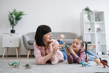 Playful tween girl with animal toy having fun with brunette woman in living room of spacious apartment. Mindful mother encouraging scientific exploration while keeping daughter entertained indoors.