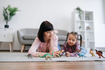 Focus on fantastic toys of extinct animals being placed on soft carpet near two involved female...