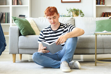 Young redhead man reading book at home
