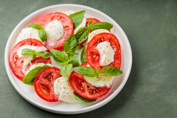 Salad Caprese with tomato, mozzarella and basil on green background. Close up