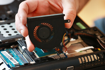 Fixing laptop. Repairman holds cooling fan and repairs from overheating. Disassembling computer,...