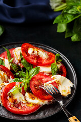 Caprese Salad. Tomato and mozzarella slices with basil leaves with fork on dark plate. Traditional Italian food
