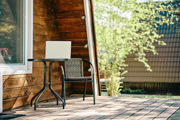 Laptop on the coffee table near whicker chair on terrace of log cabin
