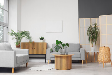 Interior of light living room with stylish grey sofas, drawers, table and houseplants