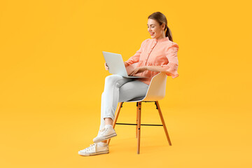 Female programmer working with laptop in chair on yellow background