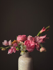 Flowers Still life. Beautiful pink flowers in vase in light on moody grey background. Stylish artistic composition of snapdragon, roses, ranunculus,gladiolus. Floral vertical wallpaper © sonyachny