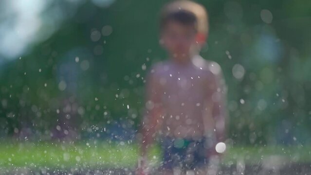 Elated child sending water jets skyward in pool on summer afternoon, small boy splashing water into the air at 120fps by swimming pool