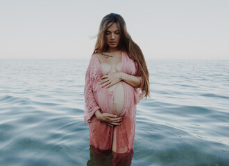 Pregnant woman in the sea holding her belly