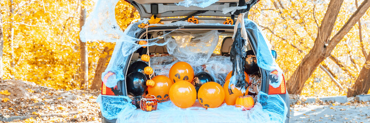cute trunk of car decorated for Halloween with cobwebs, orange balloons, pumpkins and sweets, the...