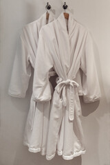 Deux robes de chambre blanche avec ceinture accrochée sur un crochet avec un support en bois devant un mur blanc