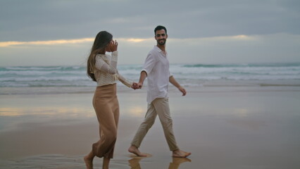 Young spouses relaxing beach at evening. Happy lovers holding hands walking