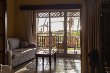 vue sur un balcon avec des chaises extérieur avec vue sur la mer et un palmier lors d'une journée ensoleillée à partir de l'intérieur d'une pièce