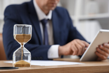 Hourglass on table of mature businessman in office, closeup