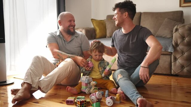 Authentic shot of young happy homosexual male gay family with adopted son toddler baby boyplay together