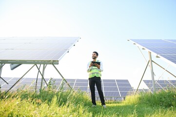 male engineer checks a photovoltaic (solar) plant and uses a recording tablet. Indian Man in uniform holding tablet.