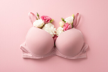 Raise awareness for breast cancer. Top view shot of bra overflowing with eustoma flowers, a representation of women's well-being, on pastel pink surface, suitable for advert or promotional content