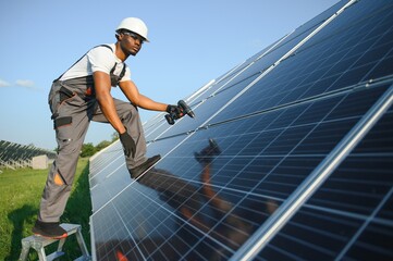African american man in safety helmet and glasses tighten nuts on solar panels with screwdriver....