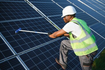 Tidy african american worker is cleaning solar panels with special broom.