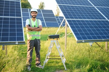 Male arabian engineer in helmet and brown overalls checking resistance in solar panels outdoors....