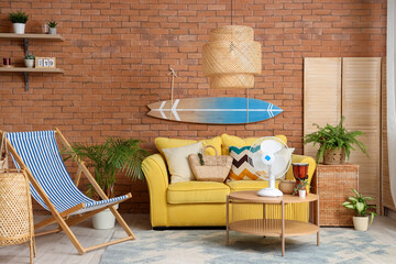Interior of stylish living room with yellow sofa, surfing board and electric fan on coffee table