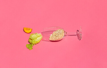 Minimal scene wine glass with oatmeal, green salad and a slice of peach. Healthy summer meal on pink background.