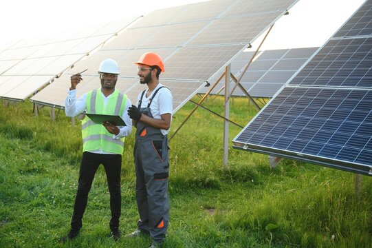 Multiracial team of engineers on solar panels. African american and arab engineer working on solar panel farm.