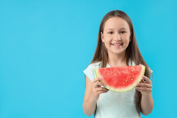 Happy little girl with slice of fresh watermelon on blue background