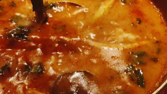 Close-up of a spoon dipping into a rich and flavourful seafood soup, made with a spicy tomato broth and loaded with fresh fish and shellfish
