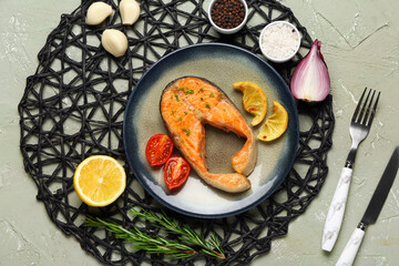 Plate of tasty salmon steak with tomatoes, garlic and lemon on grey background