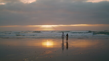 Fototapeta na wymiar Sweethearts silhouettes walking sunbeams sea. People enjoying romantic date