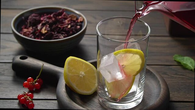 Pouring hot hibiscus tea into glass cup with lime and ice
