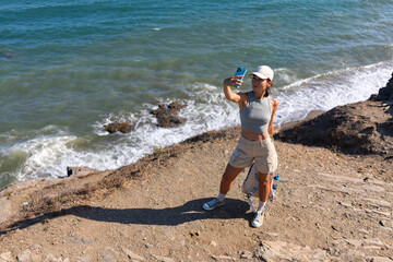 tourist girl with a backpack in the summer on top of a mountain takes a selfie against the backdrop of the sea and mountains