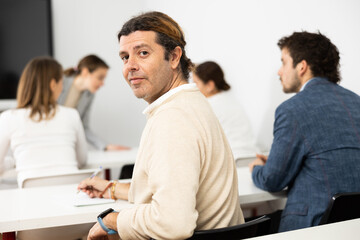Portrait of smiling man participating in psychological trainings while sitting near employees in...