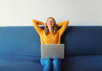 Relaxed young woman taking a break while working with laptop sitting on the couch in room at home