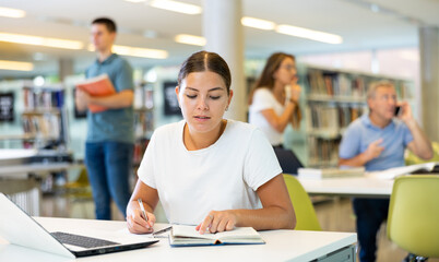 Portrait of young woman studying at library using books and laptop