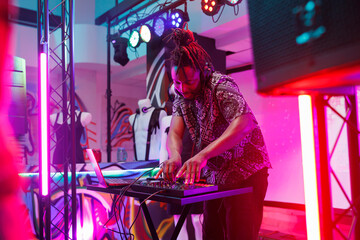 African american musician performing live on stage with spotlights at club using mixer console. Man...
