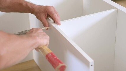 man hammers wooden pins to connect cabinet furniture parts, concept of handyman services, highlighting the skills of professionals or DIY enthusiasts who offer assembly, construction services