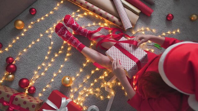 The sorceress of festive d&eacute;cor, a woman in a red dress with toys and gifts, creates a Christmas atmosphere of joy and surprises. Needlewoman of a festive feeling: a woman with a Christmas tree mouth