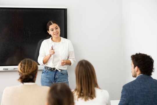 Young female professor explaining subject to classroom full of students