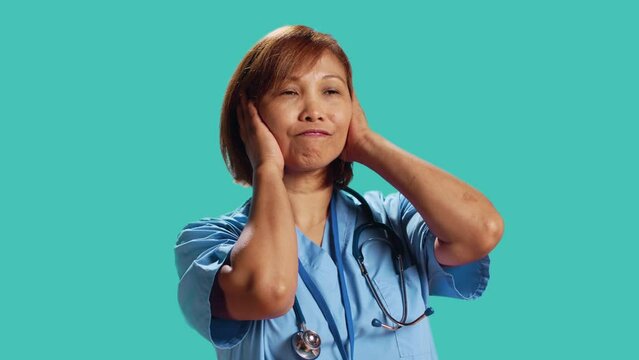 Competent nurse tormented by extreme noise while at work, close up. Healthcare employee covering ears with hands, bothered by rowdy surrounding sounds, isolated over studio background